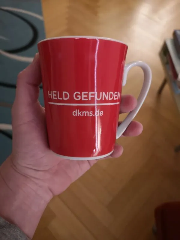 Eine rote Tasse in meiner Hand. In weißer Schrift steht dort "Held gefunden"´